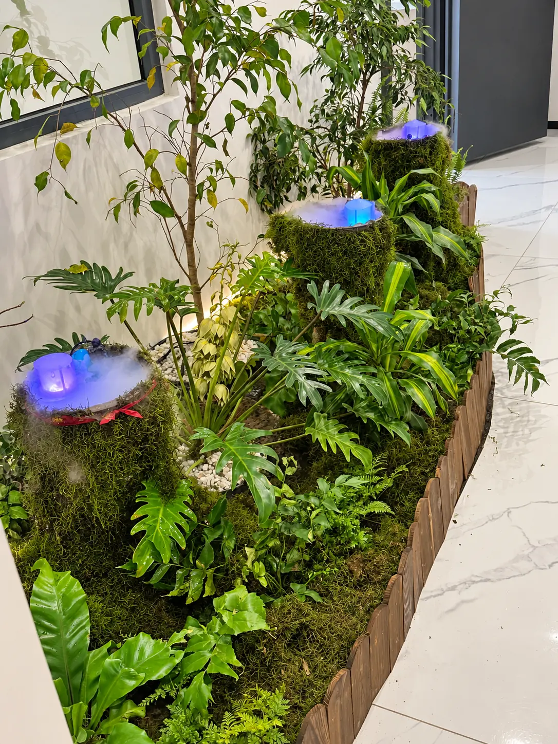 Closer view across the illuminated diffusers, moss finishes and layered foliage.