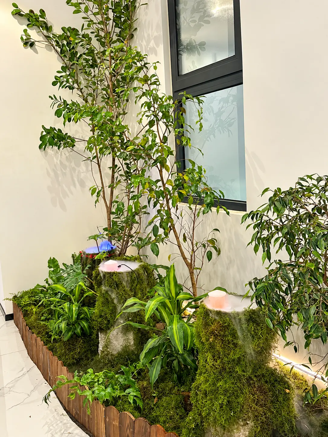 Layered tropical planting, moss-clad water features and warm linear lighting within the narrow interior.